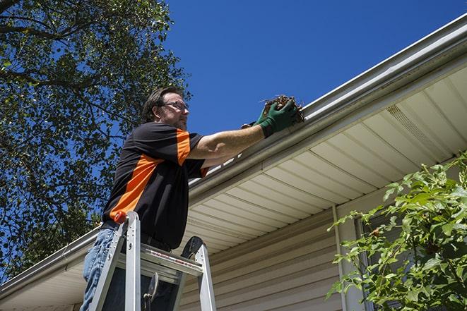 man using a ladder to fix a broken gutter in Canadian Lakes